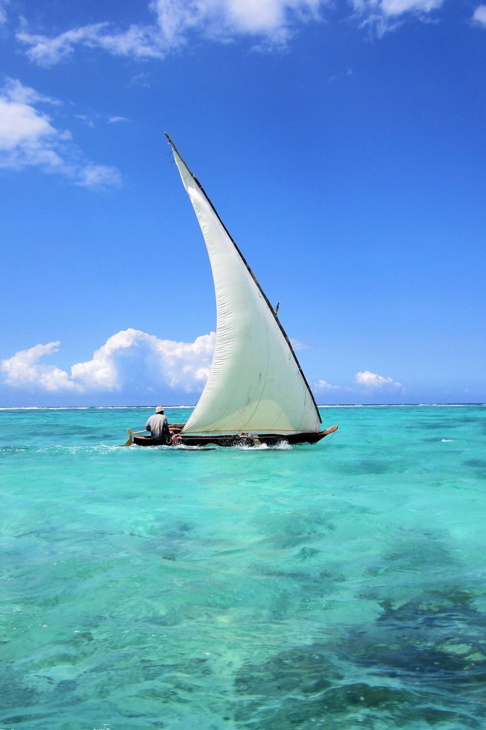 Local fisherman sailing a traditional wooden dhow on the turquoise Indian Ocean off Zanzibar.
