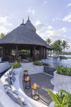 Luxury thatched-roof lounge and infinity pool with curved daybeds overlooking a palm-fringed lagoon.
