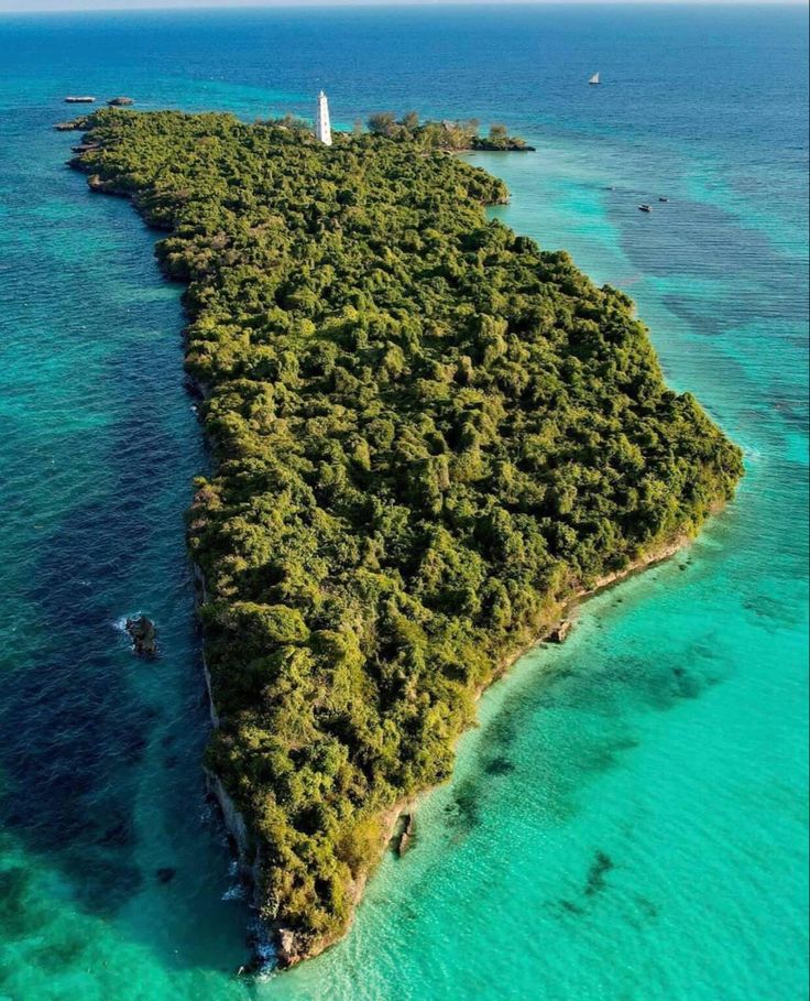 Aerial view of a forested coral island with a white lighthouse rising above a turquoise Indian Ocean reef.