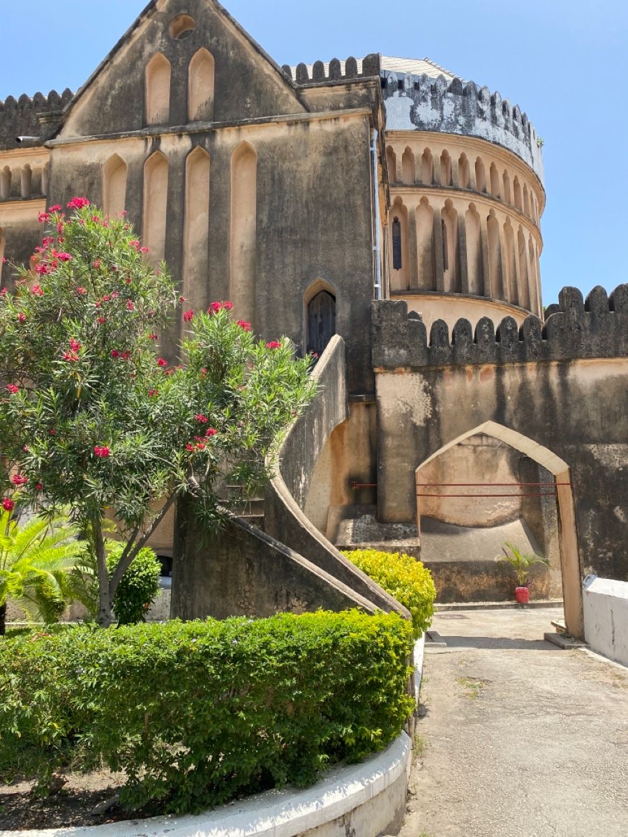 Historic coral-stone walls and crenellated turret of the Old Fort in Stone Town, framed by oleander blossoms.